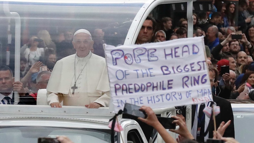 Pope Francis passes by a banner of a protester