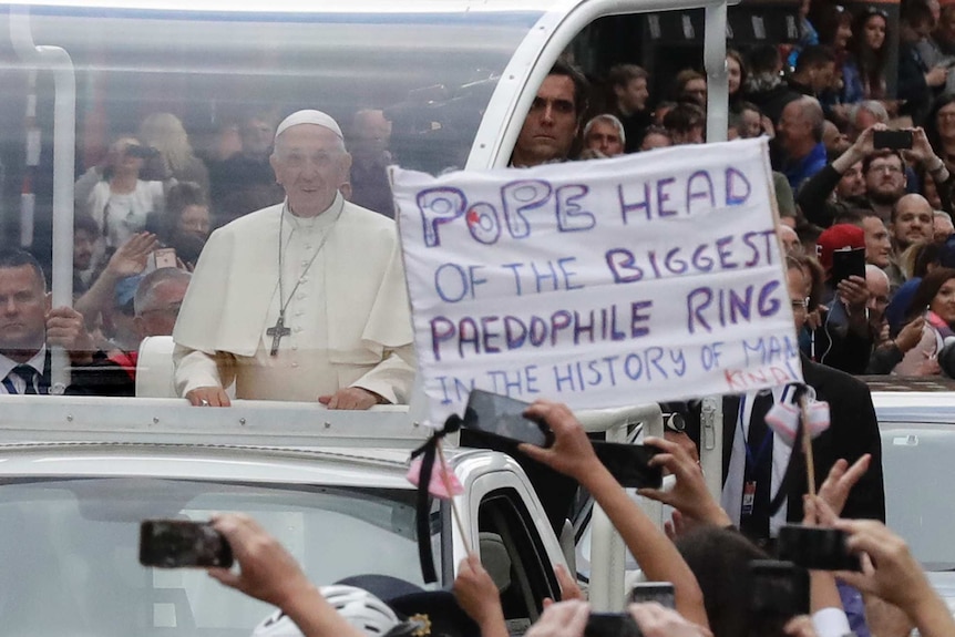 Pope Francis passes by a banner of a protester