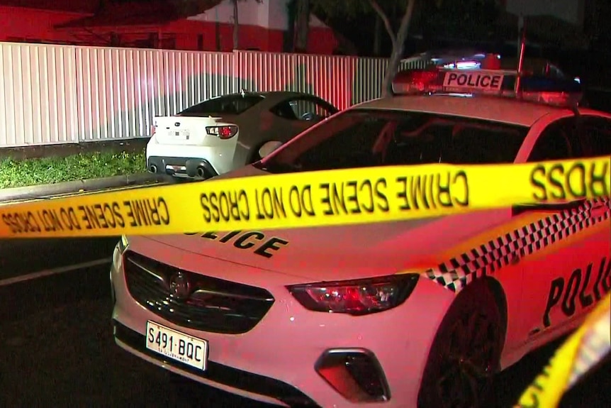 A police car and a white sports car with crime scene tape in front at night