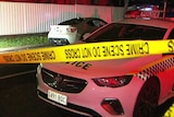 A police car and a white sports car with crime scene tape in front at night