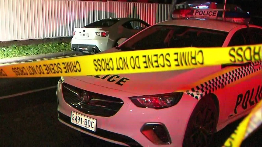 A police car and a white sports car with crime scene tape in front at night