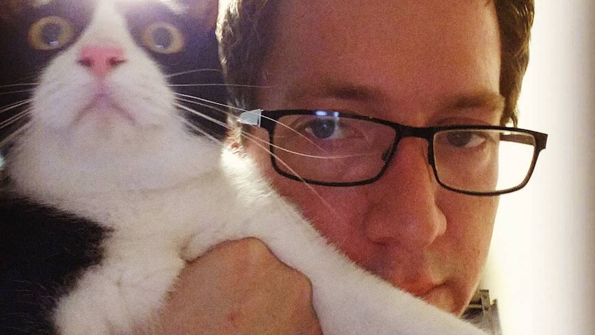 Jonathan William Parker wears glasses and holds a cat up to his face.