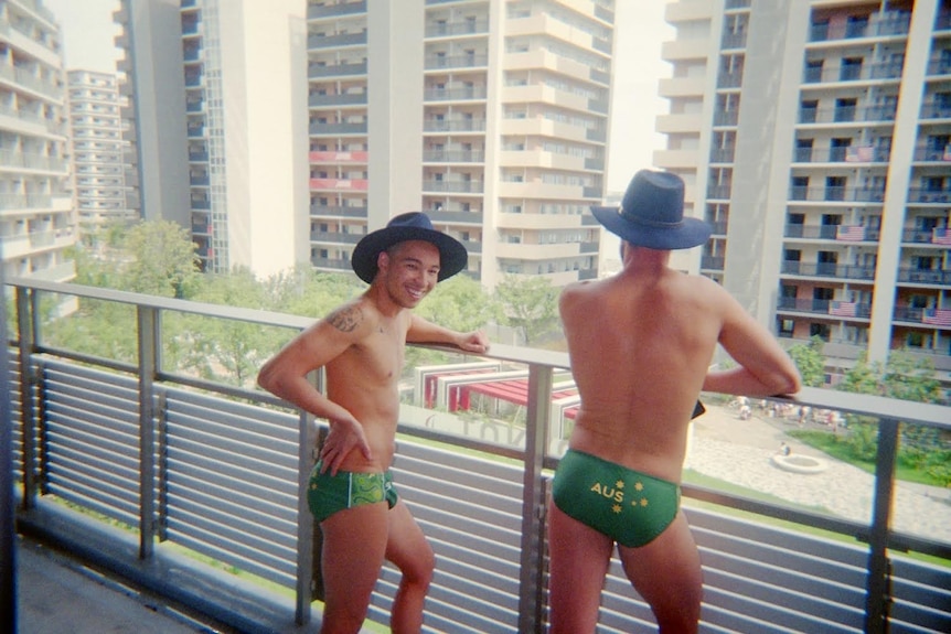 Two men standing on a balcony looking over a courtyard in budgie smugglers and akubras