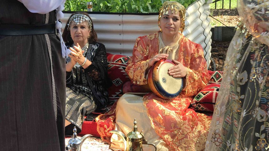 A woman plays a drum and another woman claps