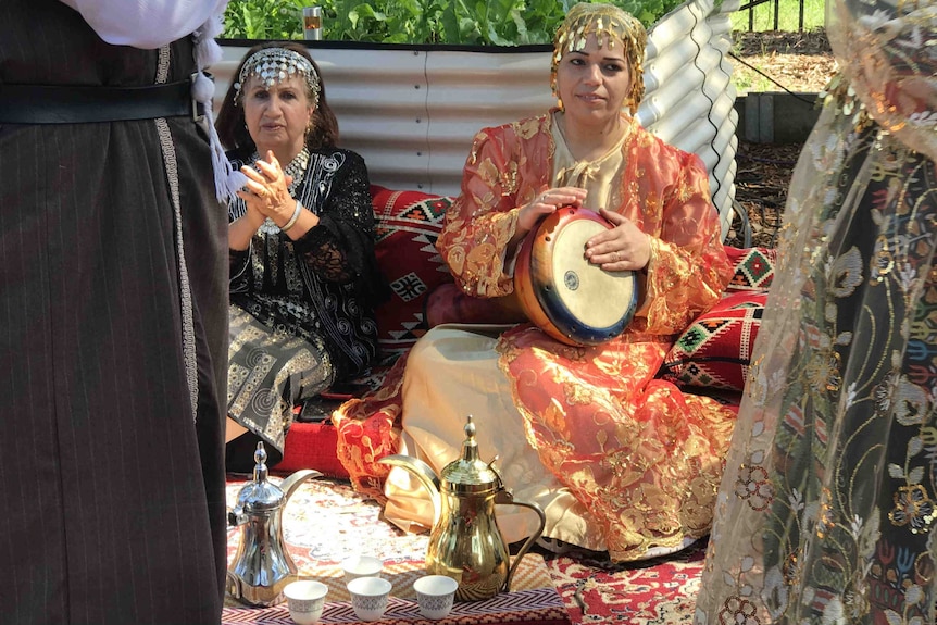 A woman plays a drum and another woman claps