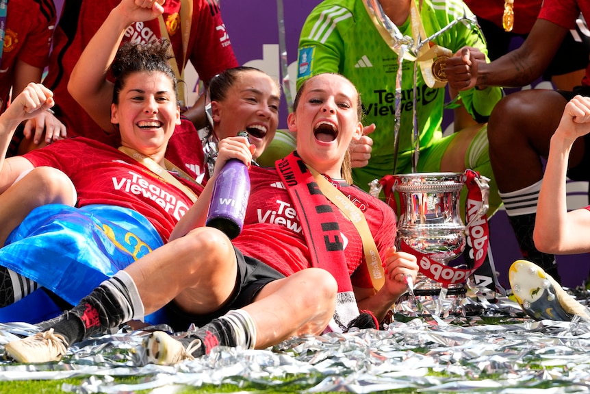 Ella Toone lies on the grass with a bottle of champagne while celebrating Manchester United's FA Cup win.