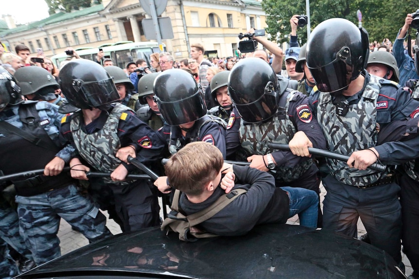 Russian police officers push a teenager against a car during a rally.