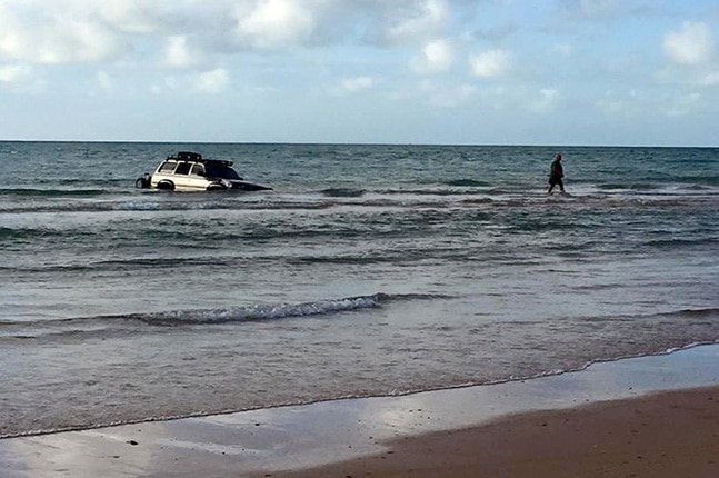 A four wheel drive being submerged off the coast of Broome as a man walks away.