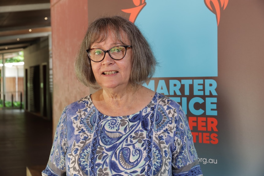 A woman with grey hair and glasses smiles at the camera. 