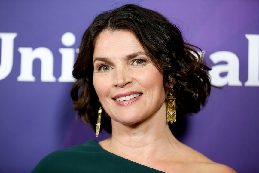 Julia Ormond smiles in front of a purple background.