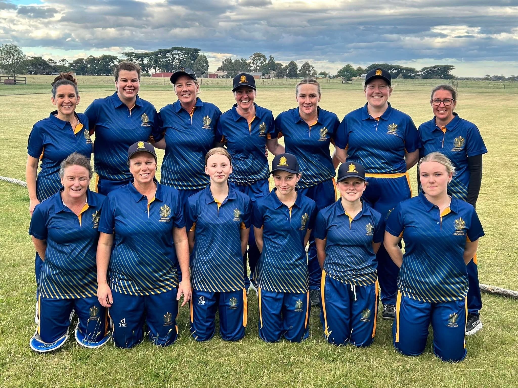 Imagem de um time de jogadoras de críquete, vestindo uniformes de críquete azul escuro. 