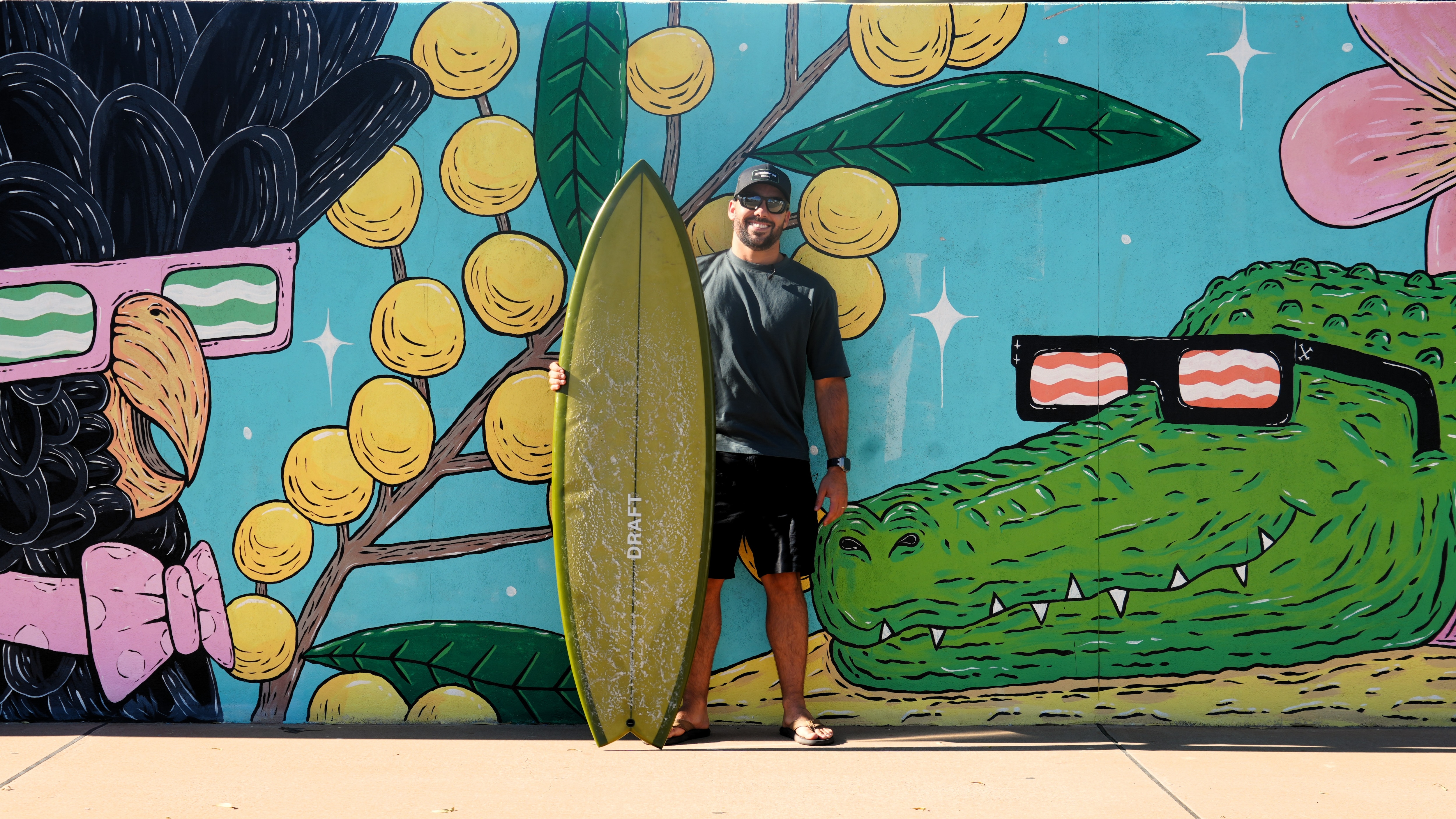pro surfer holding green surfboard in front of mural with crocodile