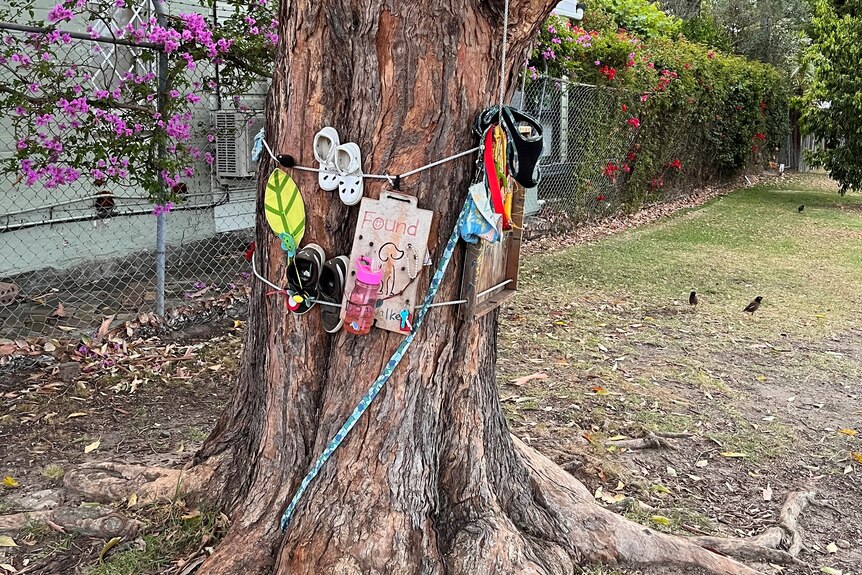 A tree with a variety of items strapped to its trunk, in cluding shoes, baby bottles an d small toys