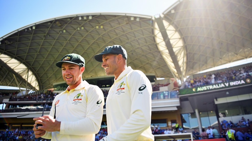 Two smiling Australian cricketers walk onto Adelaide Oval to field in a Test match wearing their Baggy Greens.