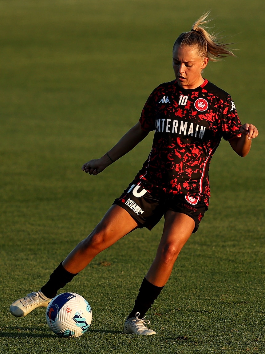A soccer player wearing red and black kicks a ball on some green grass in the afternoon
