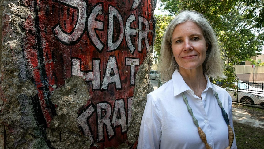 A woman stands next to a piece of concrete covered in graffiti.
