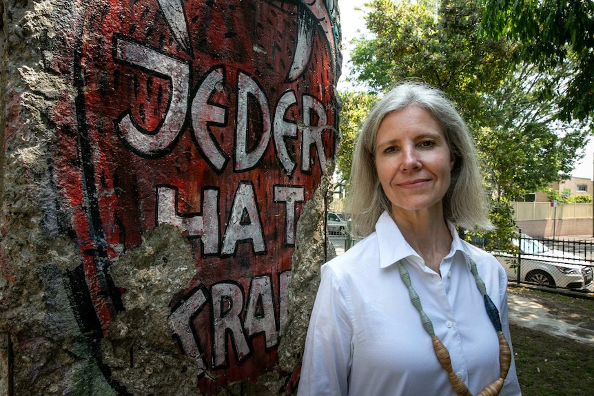 A woman stands next to a piece of concrete covered in graffiti.