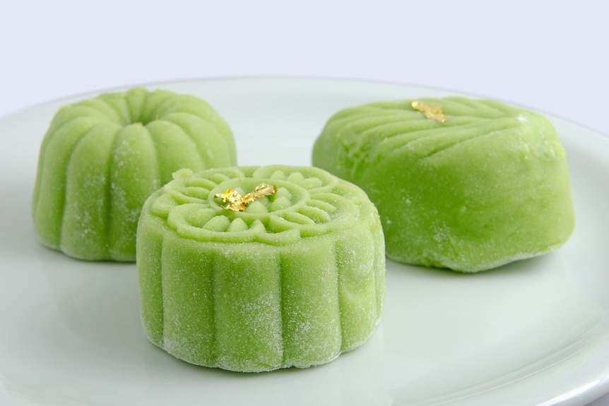 Three green coloured moon cakes on a plate.