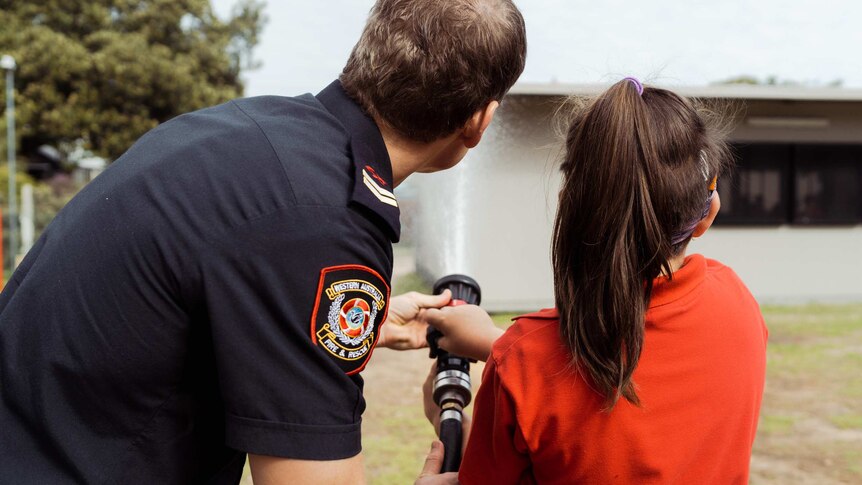 A behind shot of firefighter Michael Hatfield helping a student from Mosman Park School for Deaf Children hold a fire hose.
