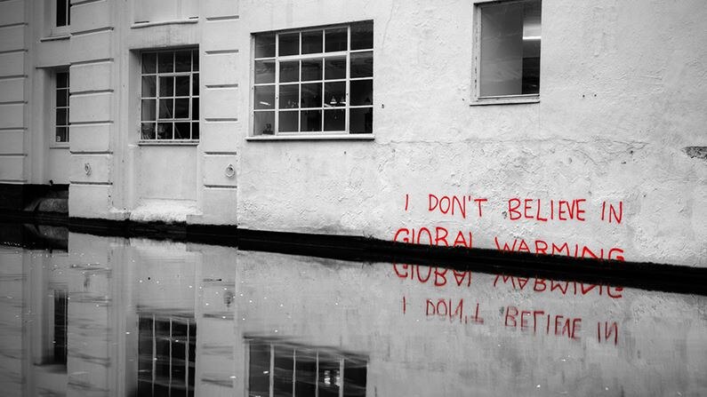 A whitewashed, stately-looking building in a flood zone with "I don't believe in global warming" written on it.