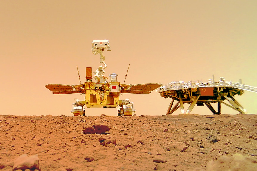 Chinese Mars rover Zhurong sits on the dusty ground near its landing platform bearing a Chinese flag.
