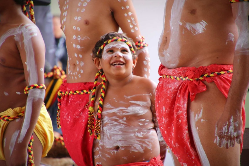 A child covered in body paint smiles and looks up at another man