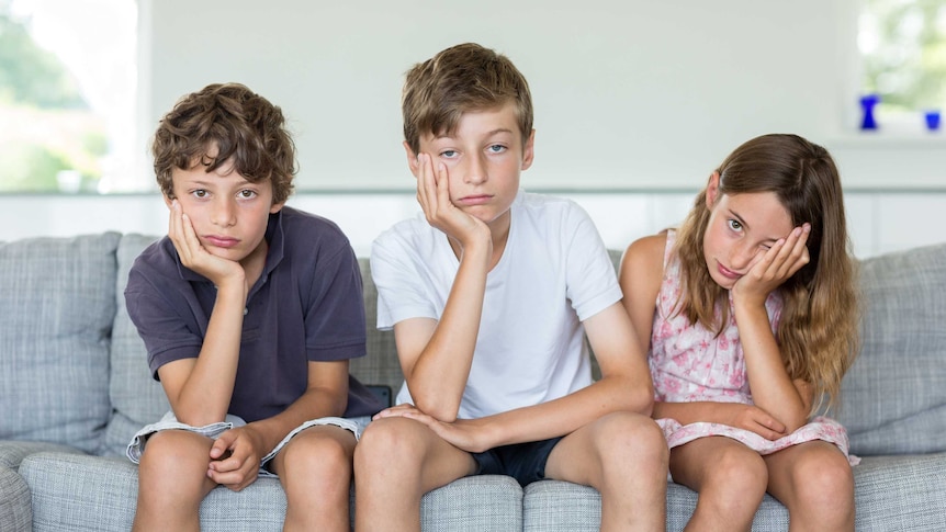 Three bored children sit on a couch