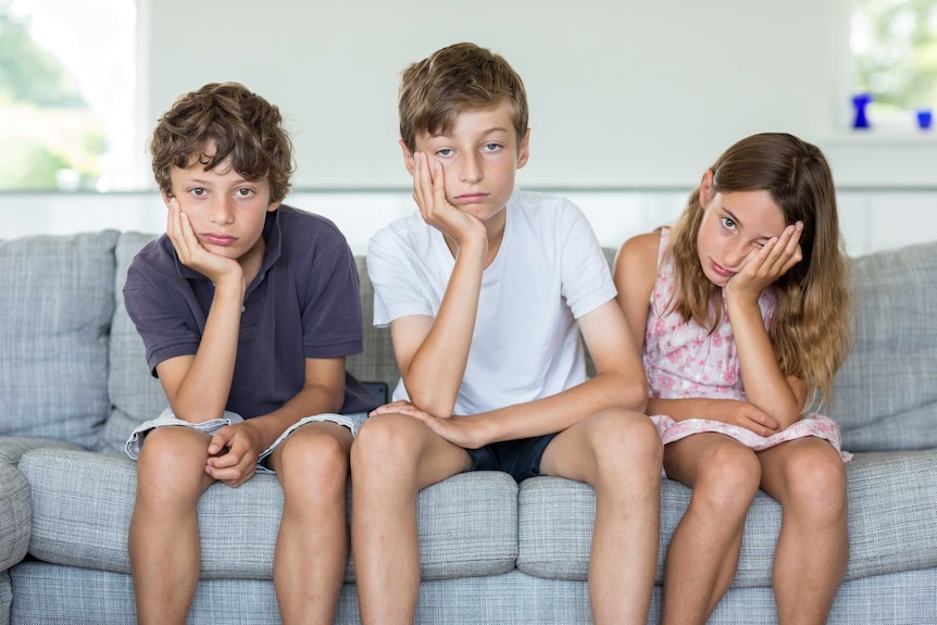 Three bored children sit on a couch