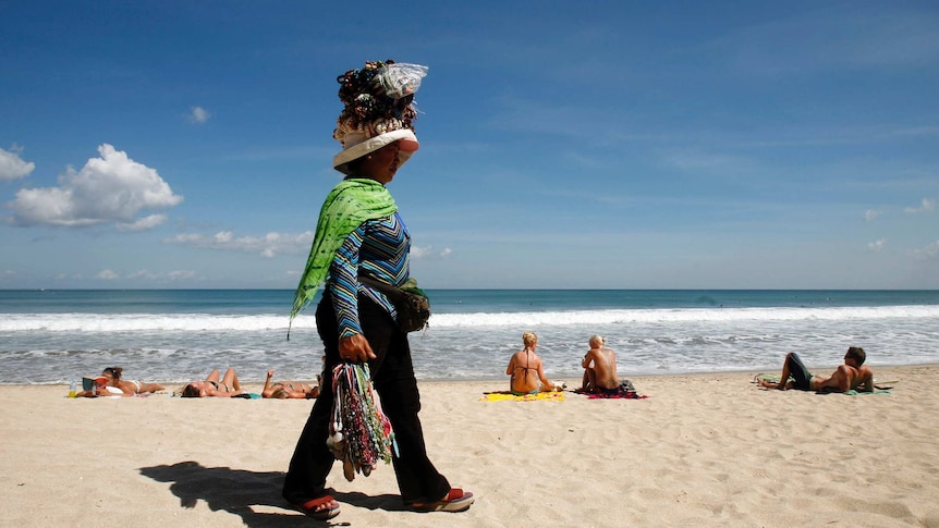 A souvenir vendor walks along Kuta beach, Bali