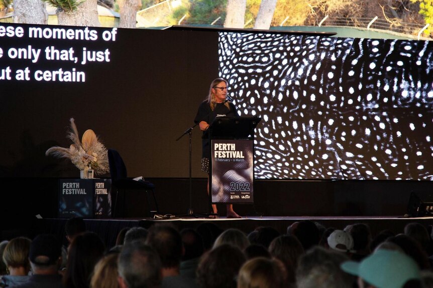 Man stands on stage behind Perth Festival podium with graphic of whale shark skin in background.