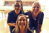 Two young women and one older woman pose together in a school hall