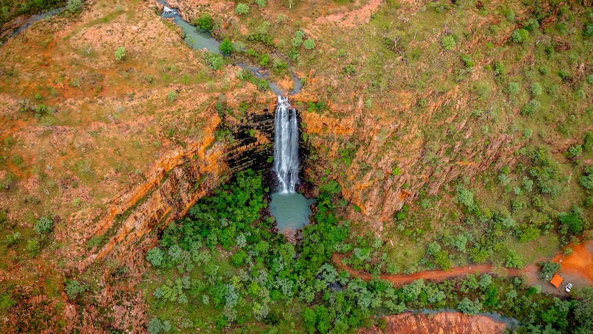 a drone image of a creek and waterfall cutting through the orange sandstone landscape