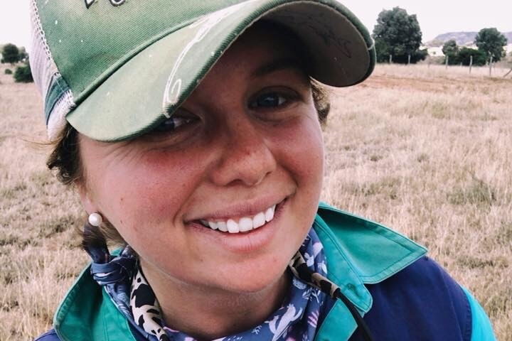 A close-up of a young woman wearing a green ball cap, standing in a paddock.