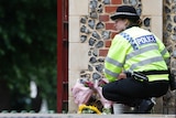 A police officer collects flowers left at the Abbey gateway of Forbury Gardens following a multiple stabbing attack in Reading.