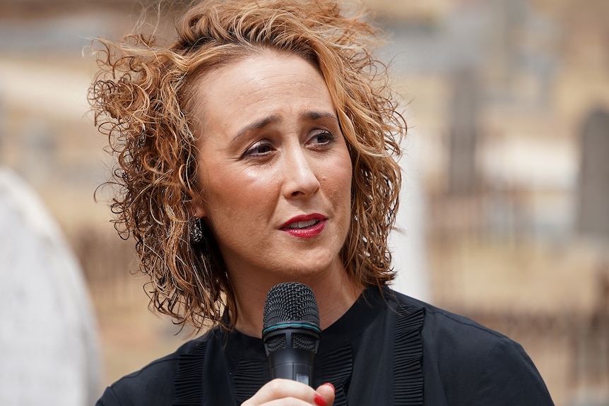 A woman with ginger hair speak to an audience at a memorial