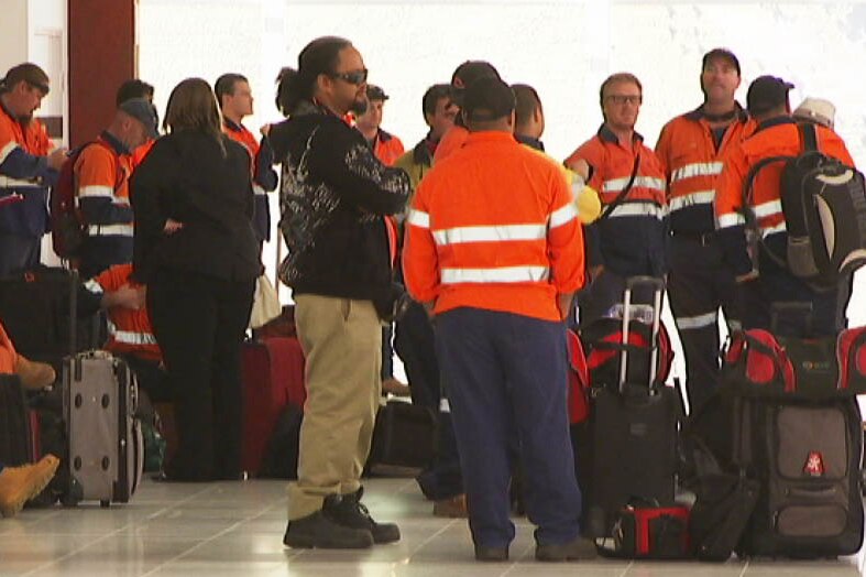 Men in hi vis clothing gather at an airport terminal.