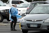 A worker in PPE holds a form as cars queue at a COVID testing clinic.