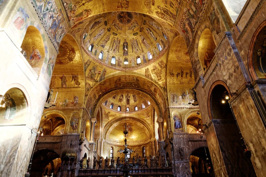 A photograph of the inside of St Mark's Basilica, featuring an ornate gold-painted ceiling