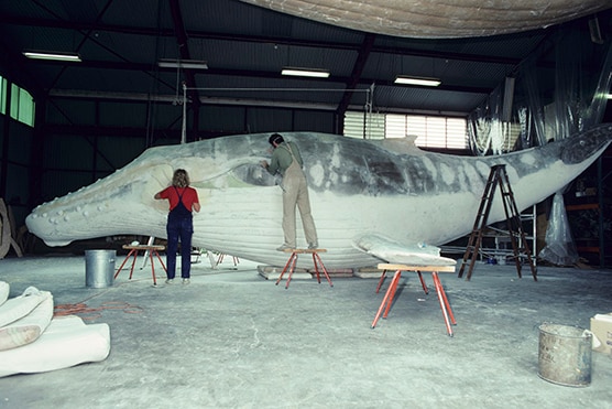 Two people painting a large whale.