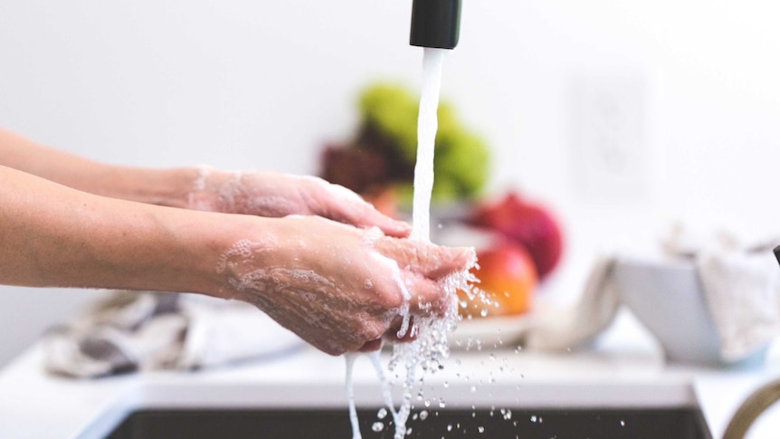 A person is washing their soapy hands under the tap in the kitchen