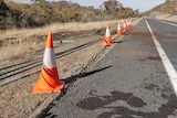 Traffic cones line the side of a highway where a barrier has been taken out.