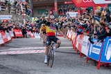 A Belgian cyclist sits up in the saddle and raises his fist in the air in celebration after crossing the finish line.