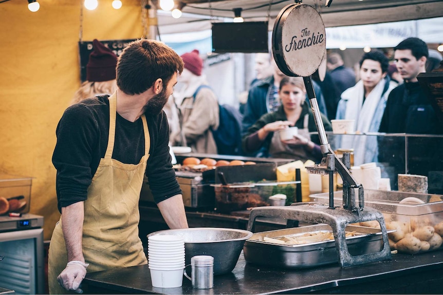 A man in an apron at a market stall standing alone to depict how to deal with feeling lonely and isolated.