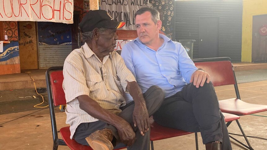 An old Aboriginal man sitting next two a white man in a suit and talking