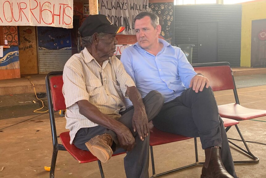 An old Aboriginal man sitting next two a white man in a suit and talking