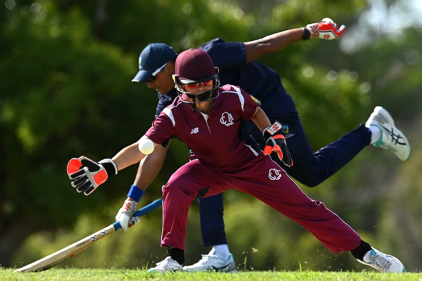 The wicket keeper goes to catch the ball while a batter reaches for the crease.