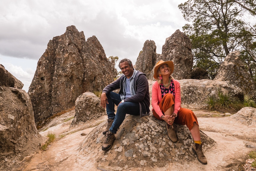 An Aboriginal man in his late 40s and a white woman in her early 40s sitting on a rock on a beach