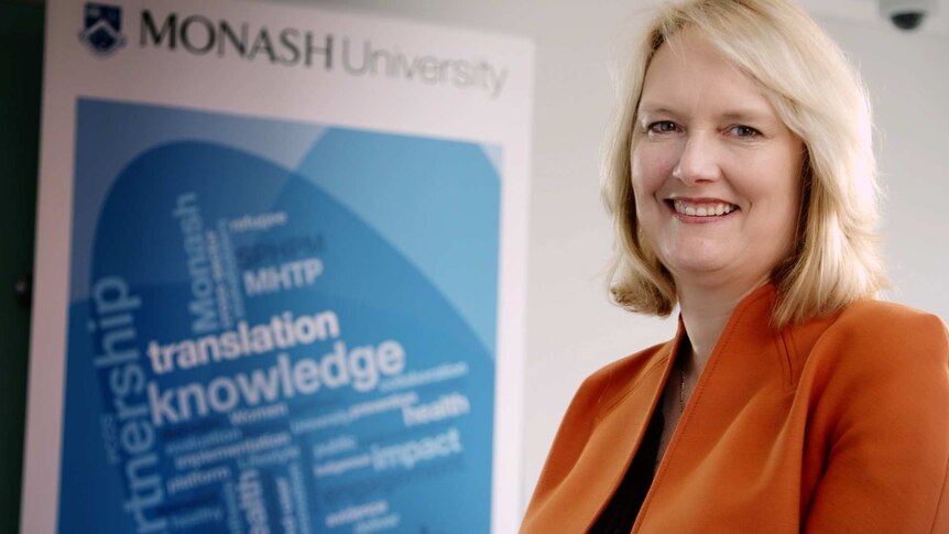 Professor Helena Teede stands in front of a Monash university promotional banner