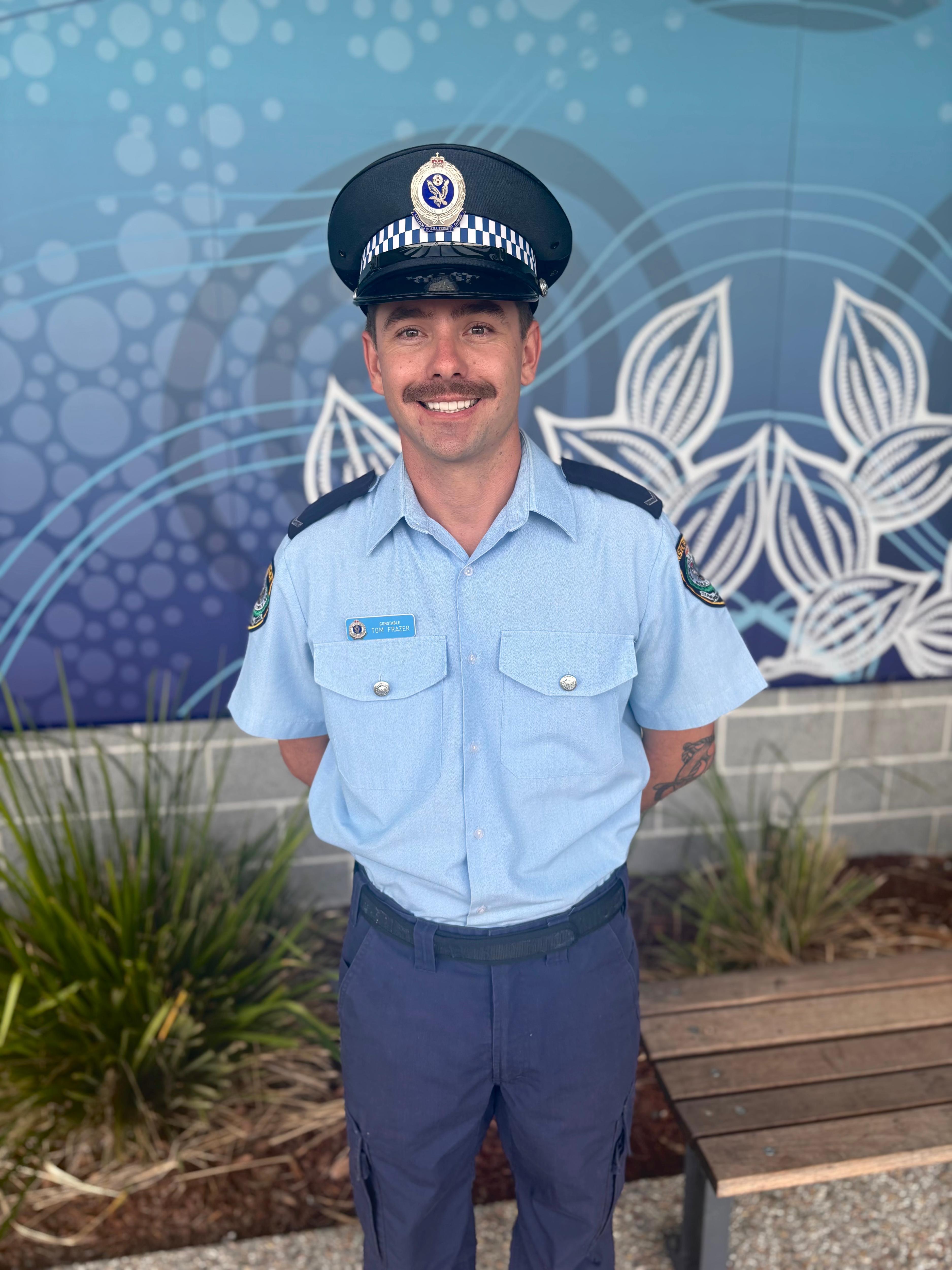 A police officer in uniform and hat standing in front of a colourful wall mural.