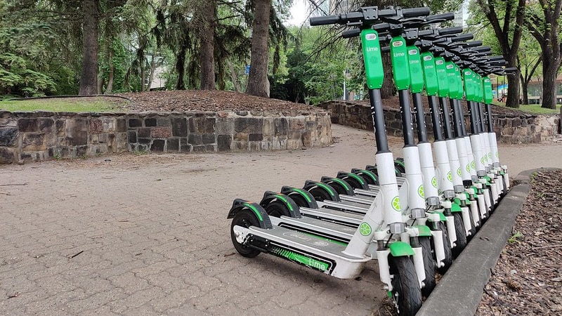 Electric scooters all the same colour and make, lined up in a rack along a path.